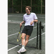 Man leaning on tennis court wearing white t-shirt and black lounge shorts.