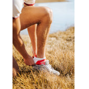 Close up shot of man putting on shoe wearing white/red performance ankle socks.