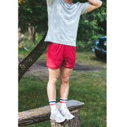 Man standing on a tree stump wearing gray shirt and burgundy lounge shorts. 