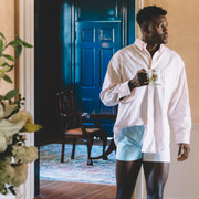 Man standing in home holding coffee mug wearing light pink dress shirt and color block slim fit boxers. 