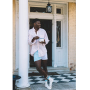 Man standing in front of open door of home holding a bowl and spoon wearing light pink dress shirt and color block blues slim fit boxers.