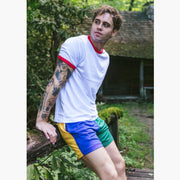 Man leaning against wooden railing wearing white t shirt and yellow/blue/green mesh lounge shorts. 