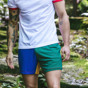 Close up of a man in forest wearing white t-shirt and blue/green/yellow multi colored mesh lounge shorts.
