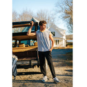 Man standing in front of car wearing sleeveless grey shirt and black lounge pants.