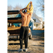 Man taking off shirt in front of car wearing black lounge pants.