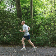 Man running in a forest wearing grey tshirt and navy blue lounge shorts.
