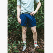 Close up shot of man standing in forest with hand on hip wearing grey tshirt and navy blue lounge shorts.