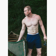 Shirtless man in forest pulling a canoe wearing navy blue lounge shorts.