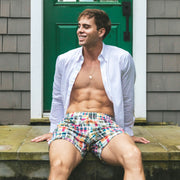 Man sitting on house porch wearing opened dress shirt and Madras printed lounge shorts.