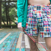 Close up of man on wooden court holding racket wearing madras print lounge shorts.