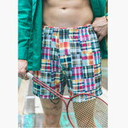 Close up shot of man wearing Madras print lounge short, opened green dress shirt, and holding a racket.