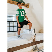 Man standing on bed wearing green jersey and white/green crew socks with letters Nila on them