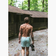 Back short of man walking next to cabins holding sandals and wearing white mesh shorts.