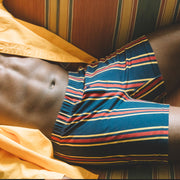 Close up shot of man sitting on couch wearing open yellow dress shirt and green/blue/red stripe slim fit boxers.