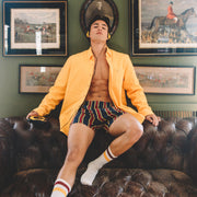 Man sitting on couch wearing open yellow dress shirt and yellow/blue/red stripe slim fit boxers.