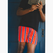 Man holding book wearing black shirt and red/blue/yellow stripe slim fit boxers.