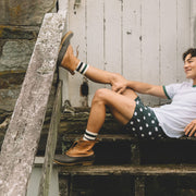 Man sitting on wooden steps wearing white shirt, boots and green slim fit boxers with white dots.