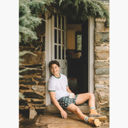 Man sitting on porch holding coffee mug and wearing white shirt, boots and green slim fit boxers with white dots.