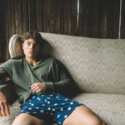 Man sitting on couch wearing green long sleeve shirt and blue slim fit boxers with white dots.