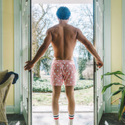 Back shot of shirtless man opening a door wearing pink slim fit boxers with white dots.