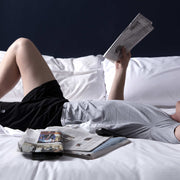 Man reading newspaper in bed wearing pocket lounge shorts.