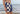Shirtless man standing next to ocean wearing checkered and solid navy blue lounge shorts.