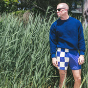 Man standing next to bushes wearing half checkered half solid blue and white mesh lounge shorts.