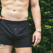 Shirtless man standing in front of bush wearing black slim fit boxer.