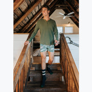 Man walking down stairs wearing long sleeve green t-shirt and green slim fit boxers with clouds, horses and trees printed on.