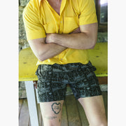 Man sitting on table with arms crossed wearing a yellow polo and black "Schooner" mesh lounge shorts. 