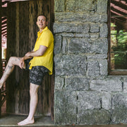 Man standing in doorway wearing yellow polo and black "schooner" print mesh lounge shorts.