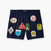 Front shot of blue 'Scout' mesh lounge short with various patch designs printed on.