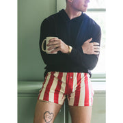 Man standing in kitchen holding a coffee mug wearing black sweatshirt and red/cream stripe slim fit boxer.