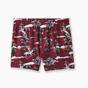 Pair of red slim fit boxers with trees and men riding horses printed on sitting against light grey background.
