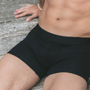Man sitting shirtless on wooden deck wearing black boxer brief.